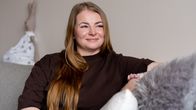 Nainen hymyilee sohvalla istuen.