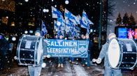 Äärioikeiston mielenosoittajia Suomen lippujen ja iskulauseiden kanssa lumisateessa.