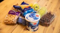 Puupöydällä lähikuvassa Milbonan kreikkalaine jugurtti, makaroonia, viinirypäleitä, cashew-pähkinöitä, kananmunia ja omenoita.