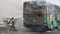 En buss står i brand. En brandman sprutar vatten på den.