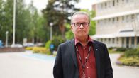 En man tittar in i kameran. I bakgrunden en parkeringsplats, hög byggnad och några buskar.