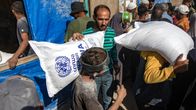Poika kantaa väkijoukon keskellä valkoista säkkiä, johon on sinisellä painettu UNRWA:n logo.