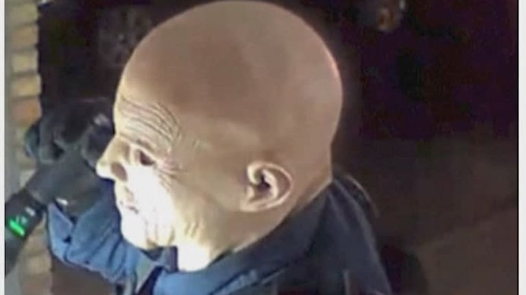 Man förklädd i latexmask och polisuniform håller i en ficklampa.