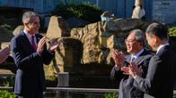 Etelä-Australian pääministeri Peter Malinauskas ja Kiinan pääministeri Li Qiang hymyilevät ja taputtavat käsiään auringonpaisteessa eläintarhassa. Taustalla pötköttelee pandakarhu.