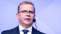 En man i kostym och slips står vid en mikrofon mot en blå bakgrund.