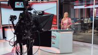 En kvinnlig redaktör står i en tv-studio. I förgrunden syns en tv-kamera.