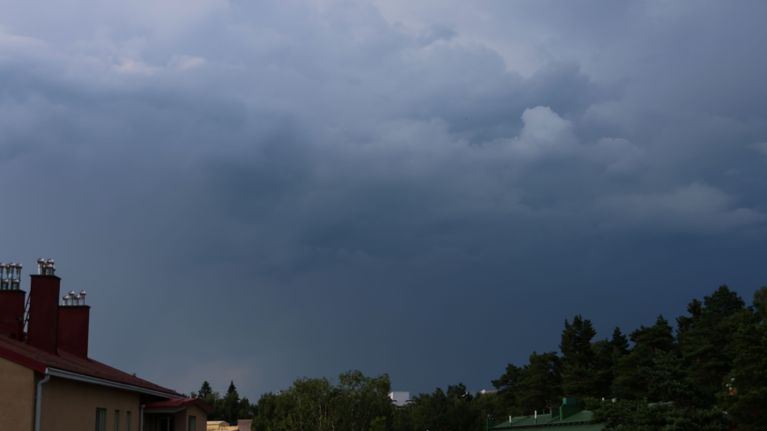 Dark rain clouds filling the sky. Rooftops and trees are seen in the bottom corners.