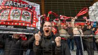 En grupp fotbollssupportrar står bakom ett nät, håller upp halsdukar och en banderoll med texten "JACKPOT"