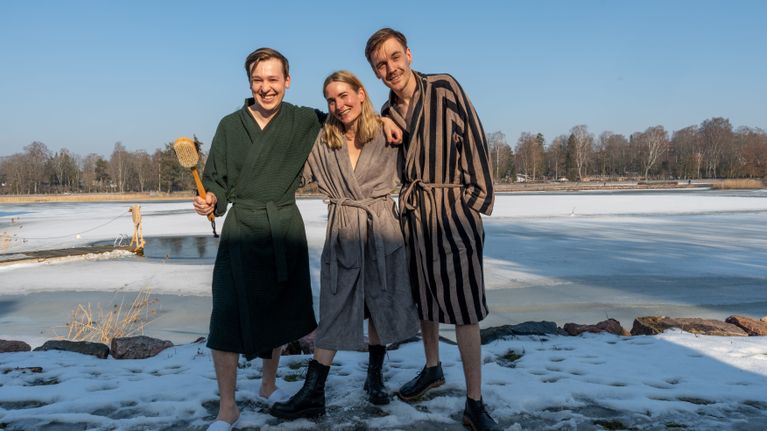 Två män och en kvinna i mitten i badrockar vid en sjö.