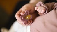 En vuxen persons hand och ett spädsbarns hand intill varandra. Den vuxna håller i en napp. 
