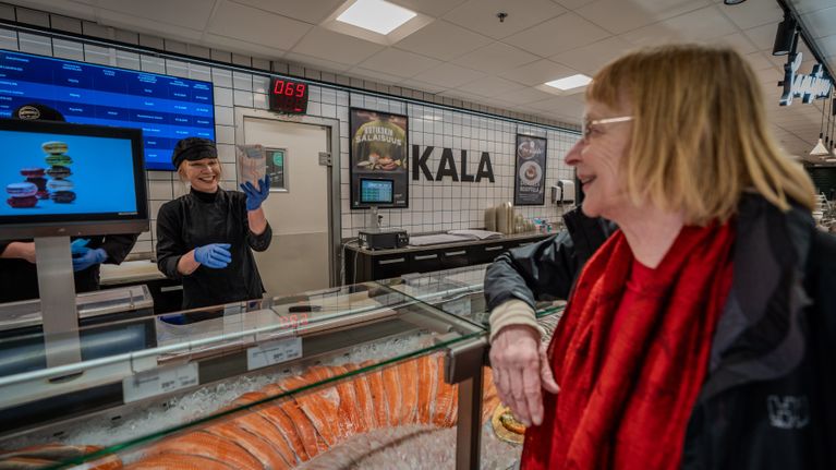 Nainen ojentaa kalapaketin asiaakkaalle.