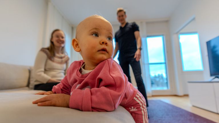 Kuvassa on pieni lapsi etualalla ja takana hänen vanhempansa.