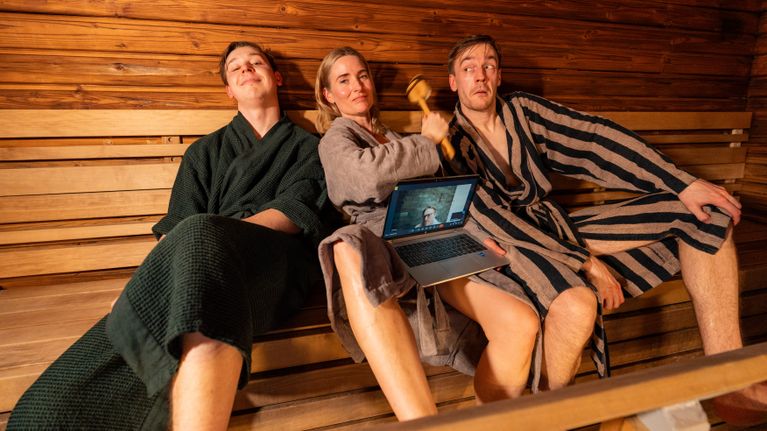 Två män och en kvinna i badrockar i bastun.