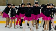 En grupp unga konståkare gör ett uppvisningsnummer på isen, klädda i svarta jackor och rosa kjolar.