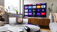A living room with a coffee table and remote controls in the foreground and a TV on a cabinet in the background.