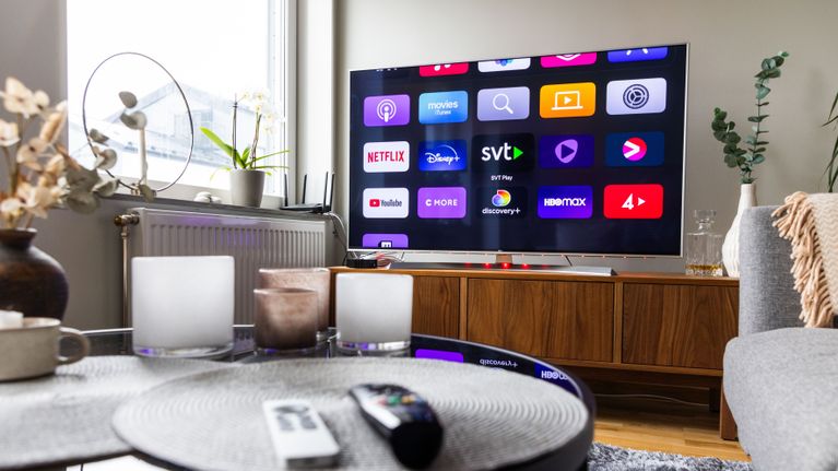 En tv med appar som Netflix, SVT och Viaplay står på en bänk i ett vardagsrum, ett soffbord syns i förgrunden.