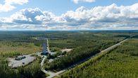 Korkea torni ja teollisuusalue erottuvat vihreän metsän keskeltä. Vieressä kulkee pitkä, suora tie kohti horisonttia.