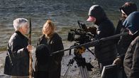 Pirkko Saisio och Alma Pöysti står vid en strand, bredvid dem syns en filmkamera och Max Smeds med sitt filmteam.