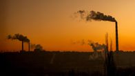 Tehtaiden piipuista nousee savua auringonlaskun aikaan.