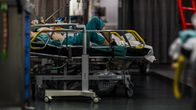 En patient ligger på en sjukhussäng i en vårdmiljö, omgiven av medicinsk utrustning.
