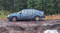 Sininen auto, jonka kylkeen kirjoitettu Riistavuori suojeluun. Taustalla metsä. 