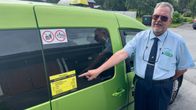 Taksiautoilija osoittaa hinnastoa auton kyljestä.