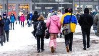 People walking through falling snow outside a shopping mall, mostly with their backs toward the camera.