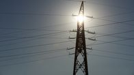 Solen tittar fram genom en ställning för högspänningsledningar. Ledningarna går åt alla håll.