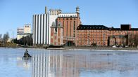En pilkare sitter på den blanka isen i dagsljus utanför academill och silorna.