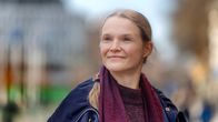 En person med ljust hår och mörka kläder står utomhus i en stadsmiljö.