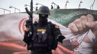 Iranin poliisin erikoisjoukkojen aseistetut jäsenet valvovat aluetta seisten panssaroidussa sotilasajoneuvossa maan lipun alla .