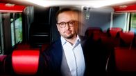 Lauri Syvänen seisoo linja-auton käytävällä punaisten penkkien keskell.