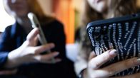 Two young women who appear blurry in the background, holding smartphones.