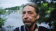 Keijo Nevaranta seisoo veden äärellä, taustalla silta ja Kajaanin linnan rauniot. 
