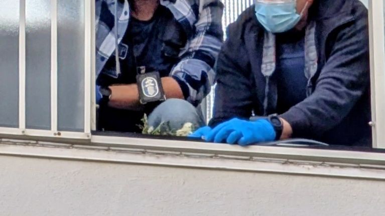 Two men in dark blue clothes and blue gloves inspecting a balcony, seen from below.