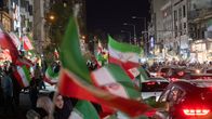Ihmiset heiluttavat Iranin lippuja kadulla, jossa ajaa paljon autoja.