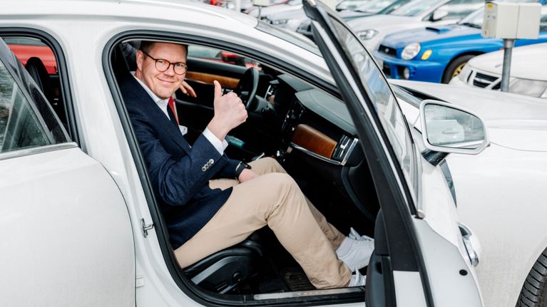 A man sits in a passenger car with the door open showing the thumbs up sign.