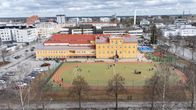 Keltainen koulurakennus ilmasta kuvattuna. Edessä urheilukenttä.