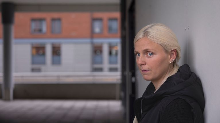 Michelle Haga står med ryggen mot en vägg och tittar mot kameran. 