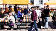 Photo shows people in a market square on a sunny day.