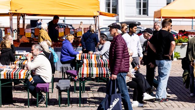 Photo shows people in a market square on a sunny day.