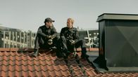 Två män, sotare, sitter på ett tak och pratar med varandra.