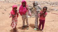 Neljä sudanilaista lasta seisomassa ulkona auringon paisteessa.