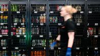 An Alepa worker, walking in front of an alcohol shelf, covered by a security shelf.