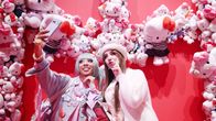 Kaksi henkilöä valokuvaa Hello Kitty -pehmolelujen edessä.
