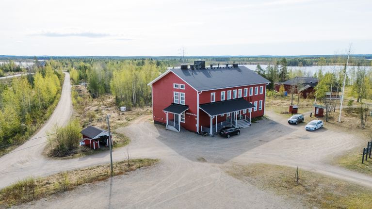 Punainen puutalo seisoo rauhallisessa maalaismaisemassa lähellä järveä.