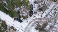 Koivupino metsäautotien reunassa. Metsäkone harventaa metsää. Työntekijän auto seisoo metsän vieressä.