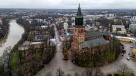 Flygfoto över Åbo med Åbo domkyrka i fokus. Den stora tegelkyrkan ligger vid Aura å, omgiven av vinterträd, grå himmel och lugna gator.