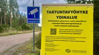 Keltainen kyltti, jolla lukee tartuntavyöhyke. Taustalla on hiekkatie ja sininen kyltti rajavalvonnasta.