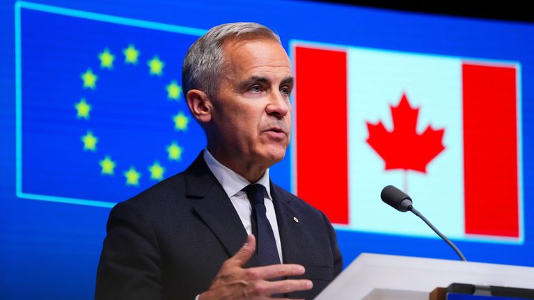 Mark Carney i en mörk kostym står vid ett talarpodium och pratar. I bakgrunden syns en skärm där EU:s och Kanadas flagga syns.